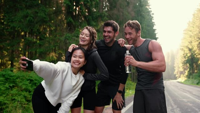 Cheerful athlete multiethnic friends taking selfies on cell phone after run on morning in the woods