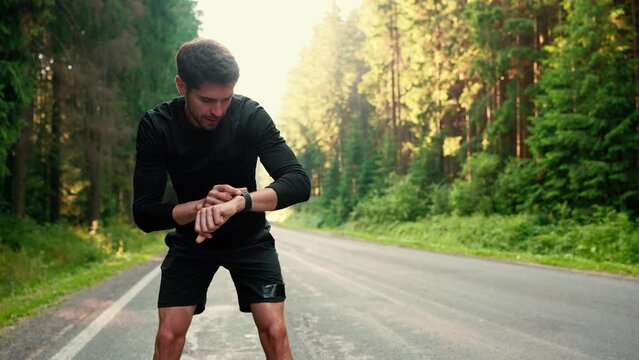 Handsome brunet sportsman stops to rest and starts jogging on morning in the forest