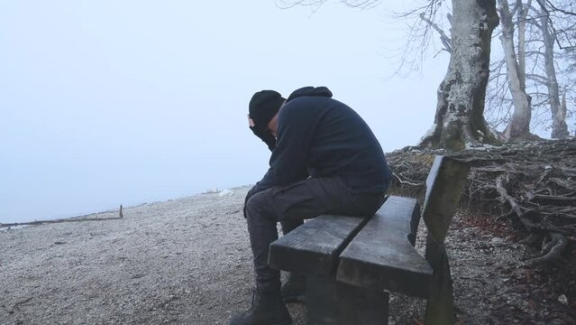 Alone depressed man sitting on the bench at the lake shoreline in foggy morning