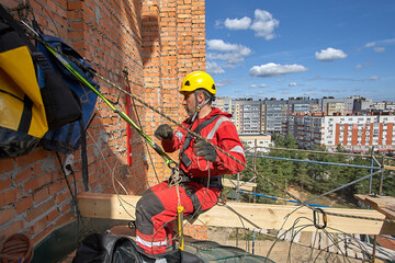 A man is working on a red brick wall. Rope access.