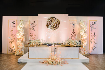 Table newlyweds in area on wedding party. Festive table, arch, wall, stands decorated composition of white, pink flowers, candles and golden decor in banquet hall. Setting table, setup, serving.
