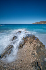 Fototapeta na wymiar clear blue sky and waves crashing on rocks shot blurry