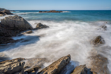 Fototapeta na wymiar clear blue sky and waves crashing on rocks shot blurry