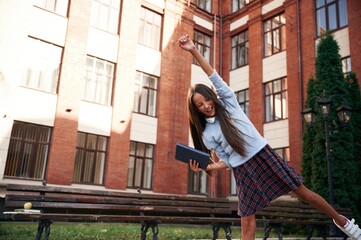 Cheerful, celebrating success. School girl in uniform is outdoors near the building