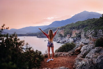 Beautiful blonde woman in casual clothes standing on the cliff near the sea 