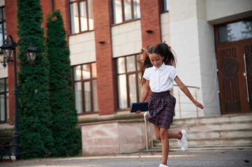 Photo in action, running. School girl in uniform is outdoors near the building