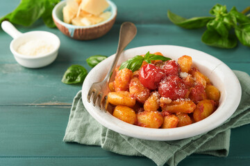 Potato gnocchi. Traditional homemade potato gnocchi with tomato sauce, basil and parmesan cheese on turquoise rustic kitchen table background. Traditional Italian food. Top view.