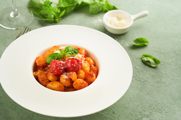 Potato gnocchi. Traditional homemade potato gnocchi with tomato sauce, basil and parmesan cheese on kitchen table on light green kitchen table background. Traditional Italian food. Top view.