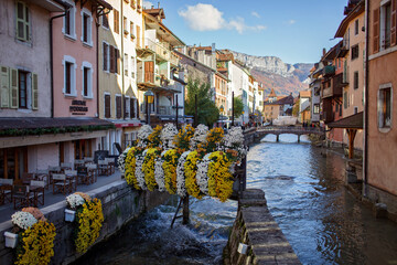 Fototapeta na wymiar A picturesque view of a narrow canal in Annecy in autumn. Quaint cafes, bridges, abundant flowers, historic houses in the medieval heart of tourist destination, France