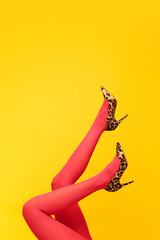 Female slender legs wearing stylish, heeled shoes with animal print and red tights over bright yellow background. Colorful photography. Concept of fashion, creativity, imagination. Copy space for ad