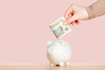 A woman's hand puts a ten dollar bill in a piggy bank. Saving money for future goals