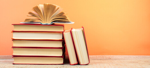 Composition with hardback books, fanned pages on wooden deck table and orange background. Books stacking. Back to school. Copy Space. Education background.