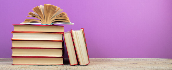 open book. Composition with hardback books, fanned pages on wooden deck table and purple background. Books stacking. Back to school. Copy Space. Education background.