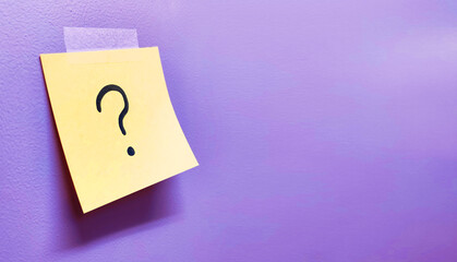 Yellow note paper with question mark on purple wall background	