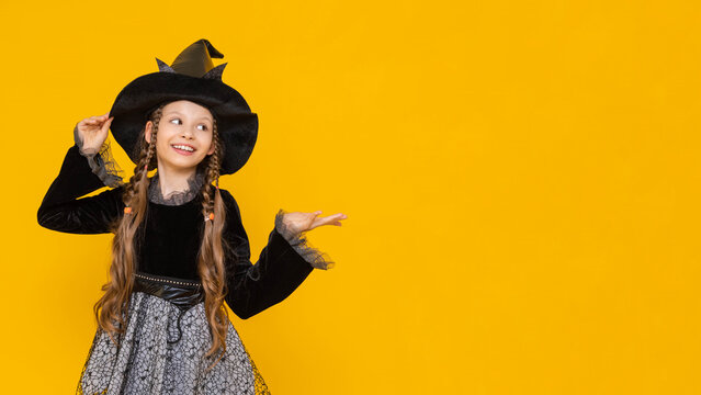 Portrait of a beautiful young witch pointing her finger to the side at an advertisement, looking into an empty space, A Sorceress in a Halloween costume on an isolated yellow background.