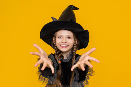 a cheerful and funny girl in a witch's fancy dress and with long pigtails, pulls her hands forward, a place for advertising with a cute witch, a witch on a yellow isolated background.