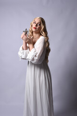 Close up portrait of beautiful blonde model wearing elegant  white halloween gown, a historical fantasy character.  Holding crucifix cross necklace, isolated on studio background.