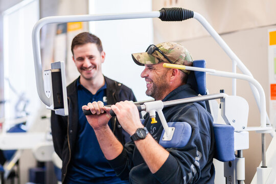 happy smiling male physio client with physiotherapist using exercise therapy equipment