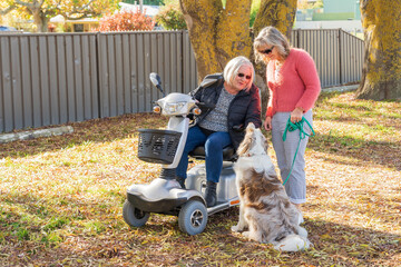 An elderly woman in a mobility scooter with her daughter and a dog in an Autumn setting