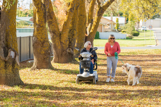 An elderly woman in a mobility scooter with her daughter and a dog in an Autumn setting