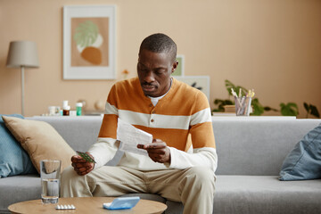 Portrait of adult African American man reading instructions for prescription pills while sitting on...