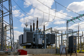 Three-phase high-voltage transformer of high electrical power at a substation against the blue sky.