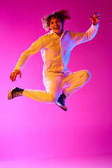 Young guy in casual stylish clothes emotionally jumping against pink studio background in neon lights. Success. Concept of human emotions, facial expression, youth, lifestyle. Ad