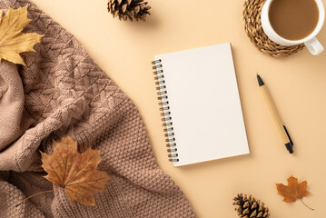Cozy fall workspace design. Top view of knitted throw, hot chocolate, spiral notebook, pen, pine cones, maple leaves on pastel beige background. Empty space for text