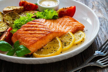 Seared salmon steak with baked potatoes and fresh vegetable salad served on wooden table
