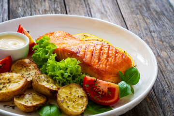 Seared salmon steak with baked potatoes and fresh vegetable salad served on wooden table
