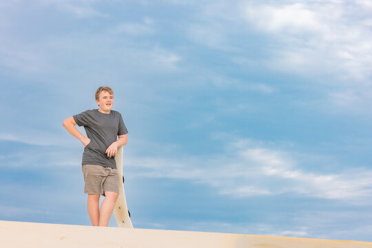 Boy standing on sand dune holding sand board on Stockton Beach