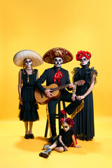 Adorable zombies posing on yellow background. Happy family with Halloween creative makeup. Celebrating for Mexican Day of the Dead. trick or treat.
