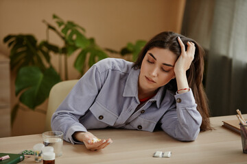 Front view portrait of depressed young woman holding handful of pills while suffering from mental health problems