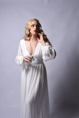Close up portrait of beautiful blonde model wearing elegant  white halloween gown, a historical fantasy character.  Holding crucifix cross necklace, isolated on studio background.