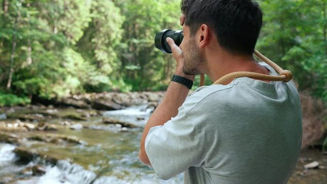 Positive man taking picture of mountain river on camera in forest 