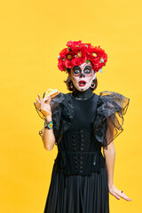 Young surprised woman in spooky makeup eating delicious hot pizza against bright yellow background....