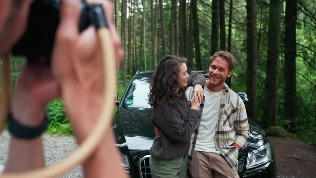 Man takes photo of lovely couple on camera near car in forest in mountains