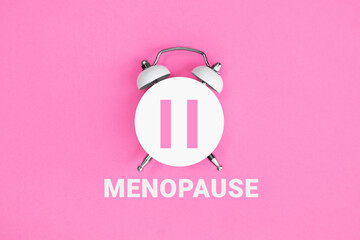 White vintage alarm clock with an inscription MENOPAUSE on pink background.