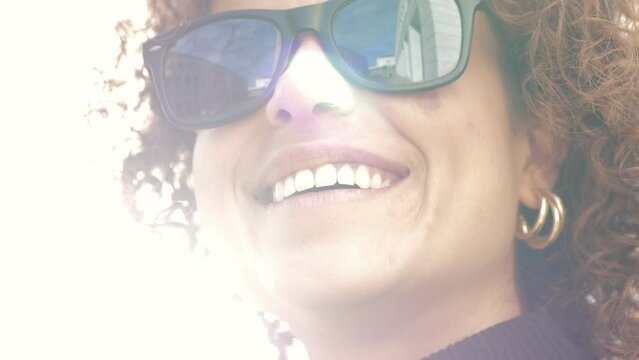 happy woman wearing sunglasses smiles in the reflected light of the sun