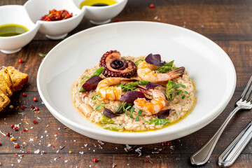 Risotto with jumbo shrimp and octopus on a white porcelain plate on wooden table. Seafood risotto