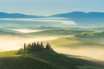 Rolgordijnen House surrounded by cypress trees among the misty morning sun-drenched hills of the Val d'Orcia valley at sunrise in San Quirico d'Orcia, Tuscany, Italy © yalcinsonat