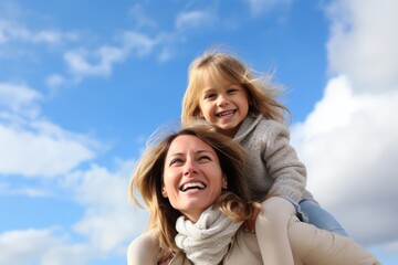 Woman giving her daughter piggyback Mother carrying daughter outdoors The little girl wraps her arms around her mother's shoulders and peeks around her head to smile