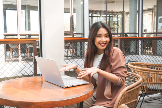 Smiling young Asian woman working remotely from cafe using her laptop, employee getting ready for online video-call interview