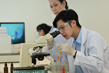 Young Asian scientist or researcher uses a microscope in study or research in the lab with...