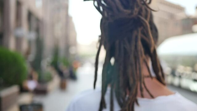 A happy man with dreadlocks happily walks around the city, dancing and swaying to the sides. A man enjoys life and is in a good mood walking in the city