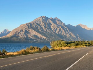 A view along the roads of Glacier National Park in Montana, United States, with the view of saint mary lake and a background full of large mountains and beautiful forests, on a sunny summer day