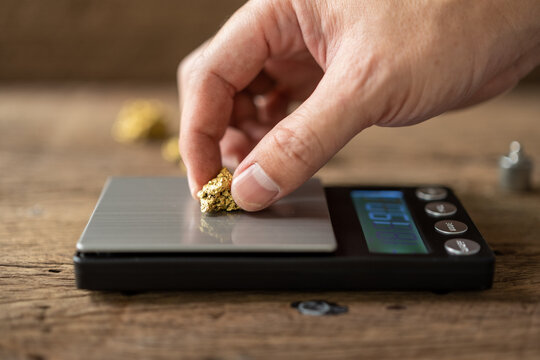 man's hand is holding a piece of pure gold mined from the mine and placing it on the weigher