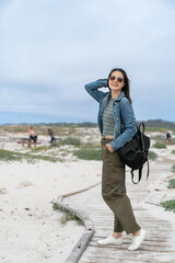 full length portrait of smiling fashionable asian female tourist posing with one hand on head and the other in pocket on the beach walkway in the breeze near California state route one