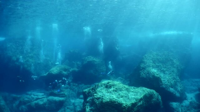  scuba divers exploring underwater topography big rocks