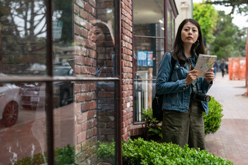 asian girl visitor looking into distance with a route map while traveling alone in Carmel by the sea. she is searching for the right way to go near a shop on the sidewalk